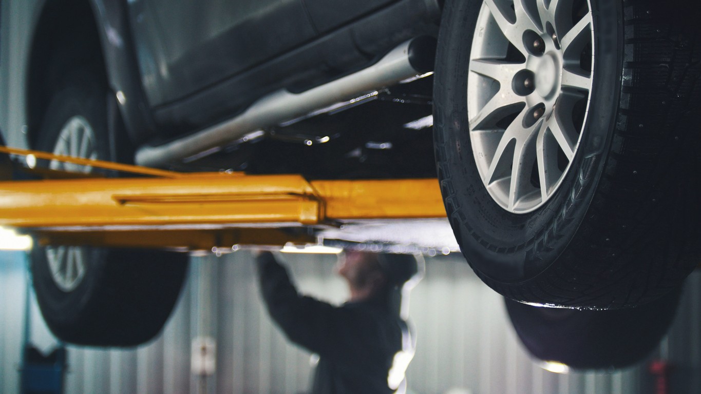 Vodič s mechanikom kontrolujú podvozok auta na zdviháku, aby odhalili skryté vady. 