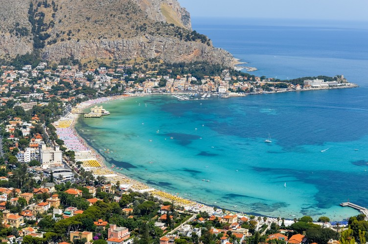 <b>Mondello – plaża w prawdziwie włoskim stylu</b>
<br>
<br>
Gdy nadchodzi lato, cała populacja Palermo pakuje plażowe ręczniki i zmierza na północ, na 1,5-kilometrową plażę o białym piasku wciśniętą między skaliste grzbiety Monte Pellegrino i Monte Gallo.
<br>
<br>
– Mondello popularność zyskała na początku XX wieku, kiedy to miejscowy arystokrata osuszył okoliczne mokradła i rozpoczął modę na budowanie okazałych willi w stylu secesyjnym przy nabrzeżu. O minionych czasach przypomina jeszcze Antico Stabilimento Balneare – olbrzymia łaźnia z przełomu wieków, której bladożółta fasada i sterczące wieżyczki wznoszą się na pośrodku plaży i wychodzą w morze – mówi przedstawiciel Rainbow. 
<br>
<br>
Nie wiedzieć, czy to przez sentyment, czy też z upodobania, od lat nad tę długą i krętą plażę o miękkim piasku, niezmiennie, tłumnie przybywają całe rodziny, miłośnicy, pływania, nurkowania, sportów wodnych i wszyscy ci, którzy cenią sobie włoską, tętniącą życiem atmosferę. Można tu spotkać zarówno turystów (choć ci wciąż są w mniejszości), jak i ludzi, którzy dopiero wyszli z pracy i chcą zrelaksować się w prawdziwie wakacyjnej atmosferze. Raczej nie mamy co liczyć na ciszę, ale ileż ten tutejszy gwar dodaje energii!