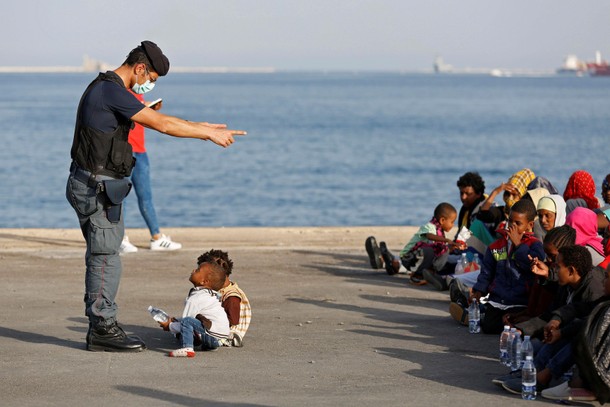 A policeman talks with children as migrants disembark from Migrant Offshore Aid Station ship Topaz R