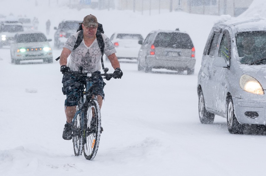 Rus vozi bicikl obučen u majicu dok je grad okovan snegom