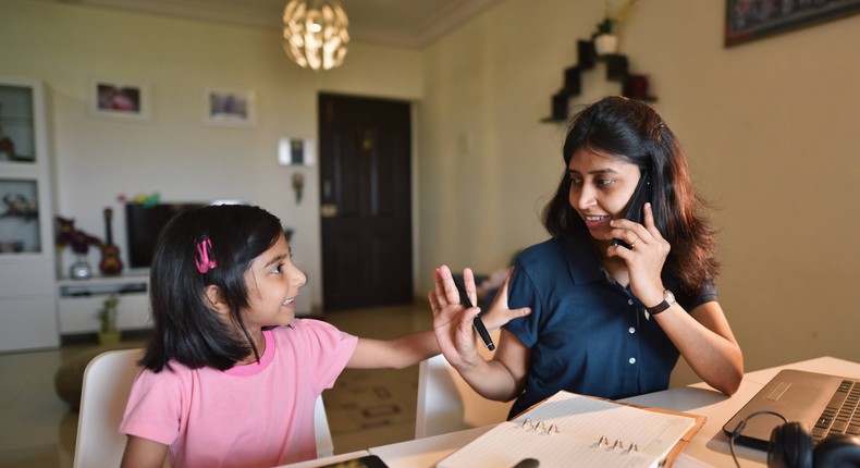 A mother is working while her daughter plays next to her on an iPad.
