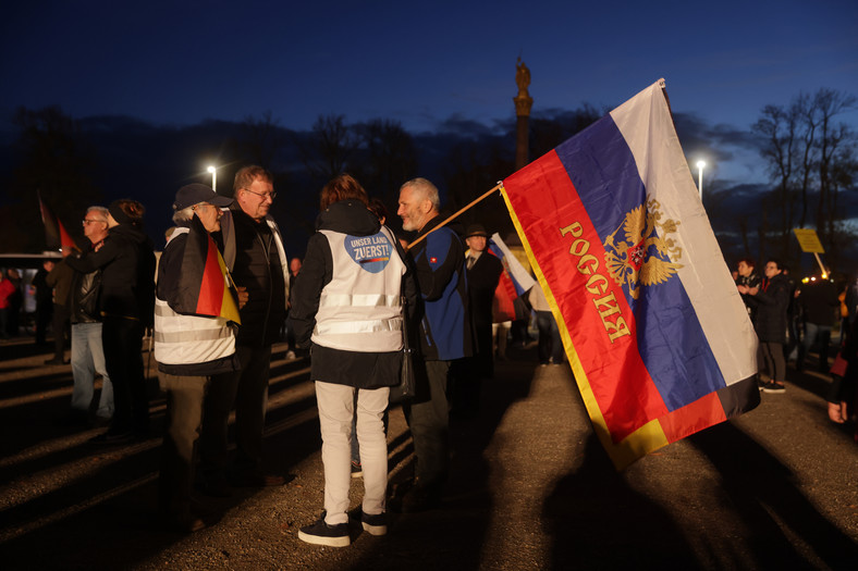 Mężczyzna w Schwerinie trzyma niemieckie i rosyjskie flagi, rozmawiając ze zwolennikami AfD przed demonstracją tej partii politycznej, 24 października 2022 r.