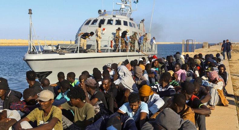 In this Tuesday, Oct. 1, 2019 file photo, rescued migrants are seated next to a coast guard boat in the city of Khoms, Libya, around 120 kilometers (75 miles) east of Tripoli. When millions of euros started flowing from the European Union into Libya to slow the tide of migrants crossing the Mediterranean, the money came with EU promises to improve detention centers notorious for abuse and to stop human trafficking. That hasnt happened