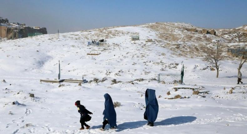 Burqa-clad women walk with a child through the snow in Ghazni province, southern Afghanistan on January 16, 2017