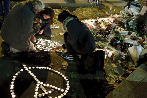 People kneel as they light candles to pay tribute to victims near the site of the attack at the Bata