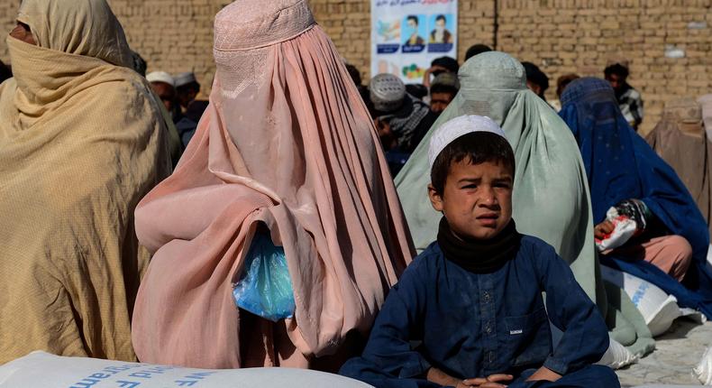 Afghan people sit besides sacks of food grains distributed as an aid by the World Food Programme (WFP) in Kandahar on October 19, 2021.
