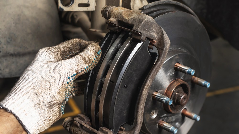 Detailný záber na brzdový strmeň a hadičku, kde mechanik hľadá stopy úniku brzdovej kvapaliny.  