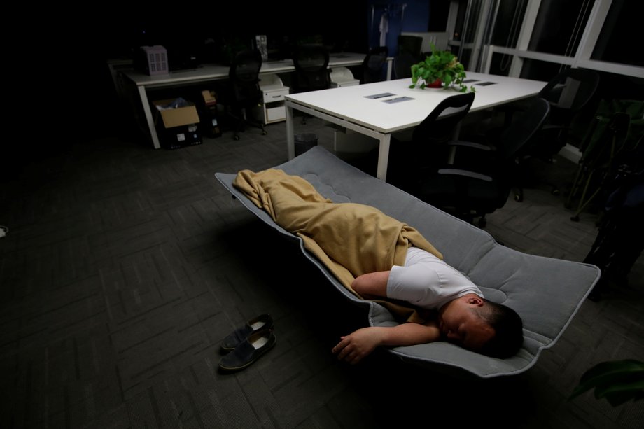 Ma Zhenguo, a systems engineer at RenRen Credit Management Co., sleeps on a camp bed at the office, after finishing work in the early morning.