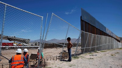 File photo of a boy looking at U.S. workers building a section of the U.S.-Mexico border wall at Sun