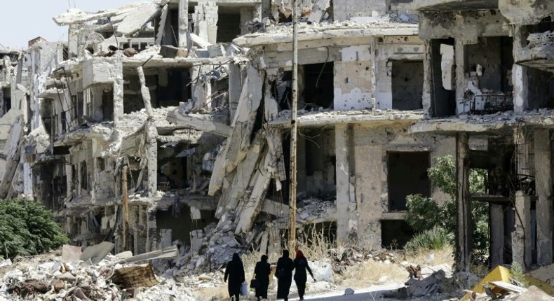 Women walk between destroyed buildings in the government-held Jouret al-Shiah neighbourhood of the central Syrian city of Homs