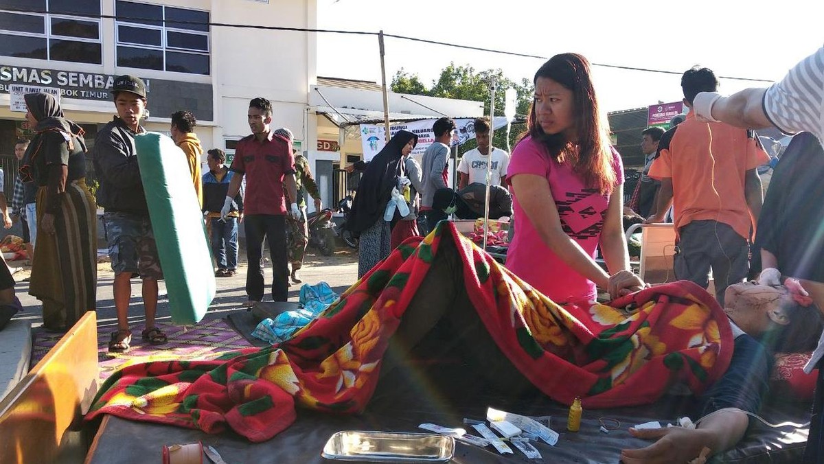 A woman stands near an injured person outside of a hospital after an earthquake hit Sembalun Selong village in Lombok Timur