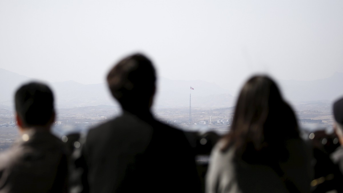 Tourists look at a North Korean flag fluttering on top of a tower at the propaganda village of Gijungdong in North Korea