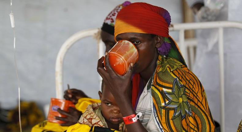 A Burundian refugee woman carries her child as she drinks from a cup at a makeshift clinic at the Lake Tanganyika stadium in Kigoma western Tanzania, May 19, 2015.    REUTERS/Thomas Mukoya