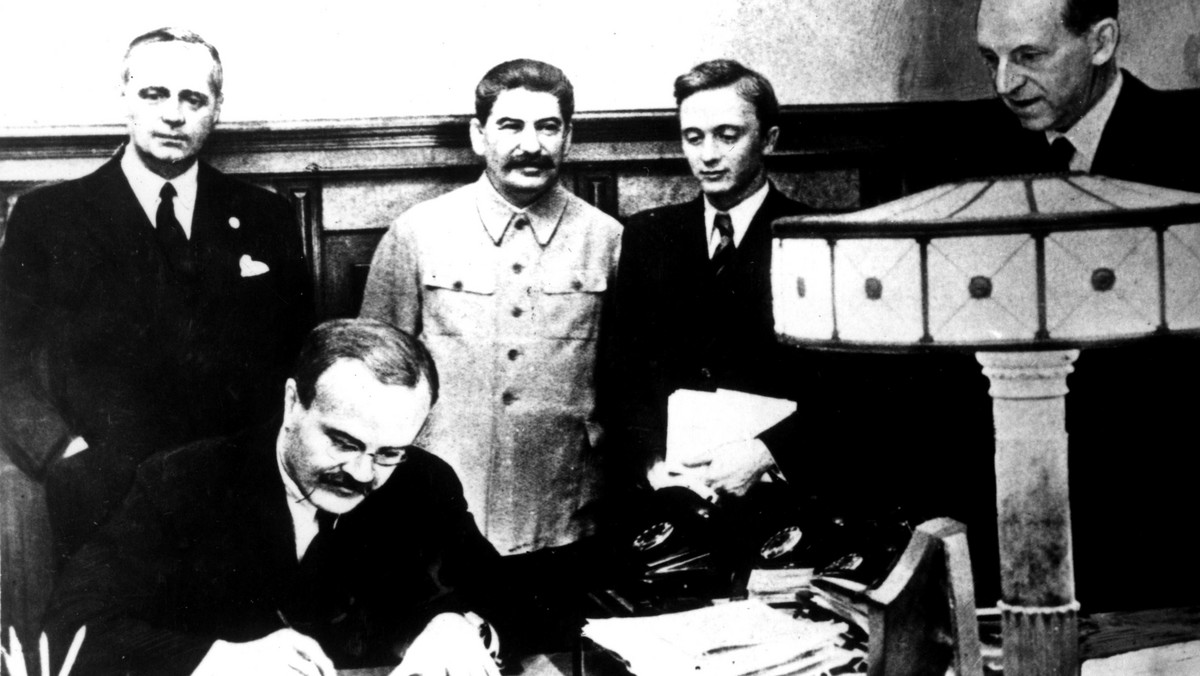 Wiaczesław Mołotow podpisuje dokument. Za nim stoją Joachim von Ribbentrop i Józef Stalin