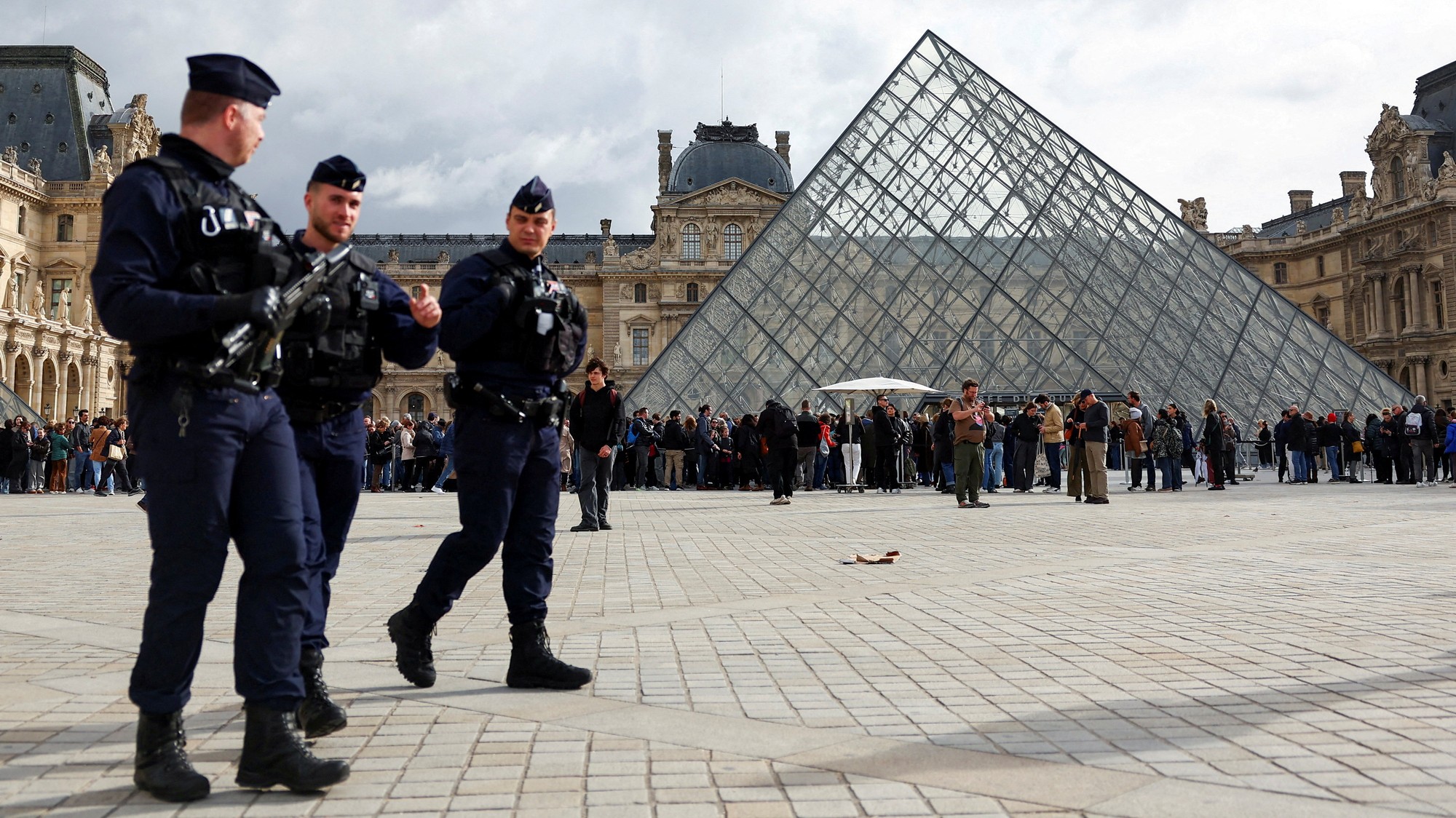 Francúzski policajti CRS v protivýtržnom výstroji kráčajú v blízkosti sklenenej pyramídy múzea Louvre.
