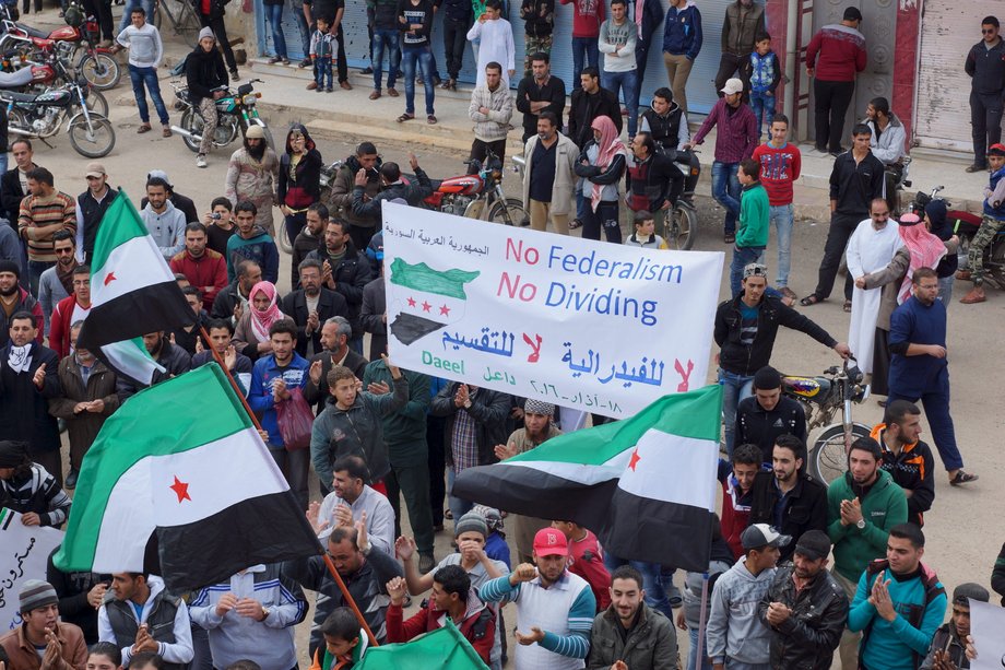 People carry a banner and wave Free Syrian Army flags while attending an antigovernment protest in the rebel-held town of Dael, in Deraa Governorate, Syria, March 18, 2016.