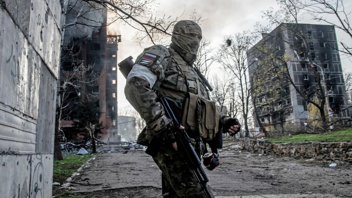 Rosyjski żołnierz stoi na tle płonącego bloku mieszkalnego w centrum Mariupola. Ukraina, 18.04.2022