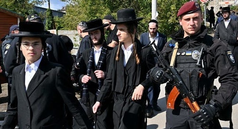 An armed police officer stays in guard as Hasidic Jewish pilgrims walk after praying at the grave of Rabbi Nachman in Uman, Ukraine.