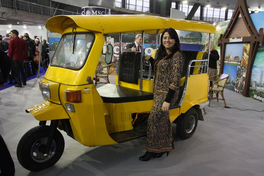 Promoterka sa štanda "Ars&co" u uniformi "Singapur erlajnsa" pored taksija "tuk-tuk" iz Bankoka