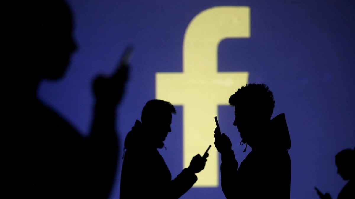 FILE PHOTO: Silhouettes of mobile users are seen next to a screen projection of Facebook logo in thi