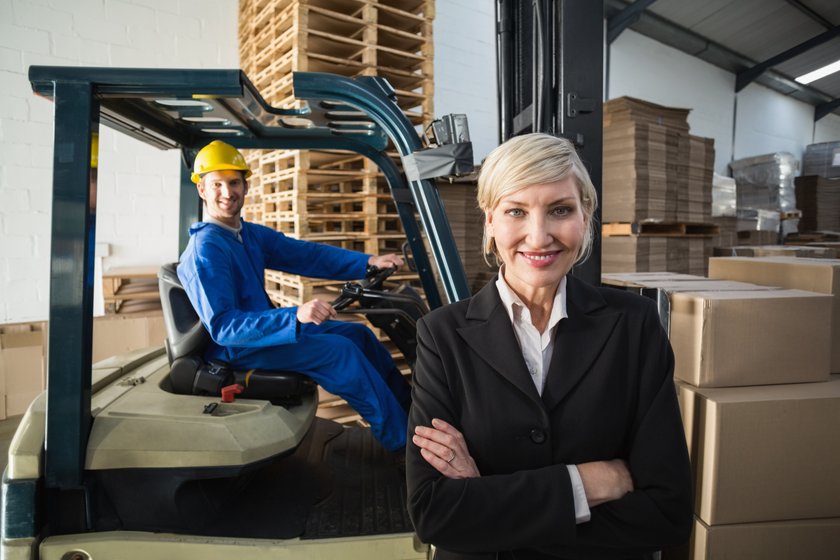 Smiling warehouse manager standing with arms crossed in a large warehouse