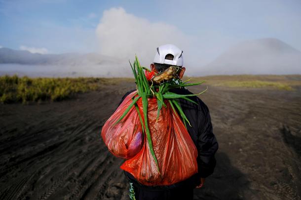 Mount Bromo spews ash in the distance as a Hindu villager carries offerings ahead of Kasada ceremony