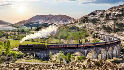 Glenfinnan Railway Viaduct in Scotland with the Jacobite steam train against sunset over lake