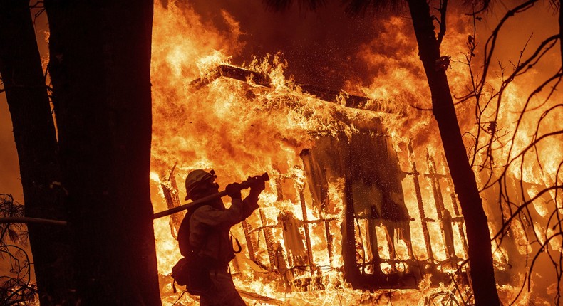 FILE - In this Nov. 9, 2018 file photo, firefighter Jose Corona sprays water as flames from the Camp Fire consume a home in Magalia, Calif. The massively expensive wildfires in 2017-2018 have prompted the creation of a five-member board, that met Wednesday April 3, 2019, to continue to consider who should pay for the increasingly destructive and costly wildfires. (AP Photo/Noah Berger, File)