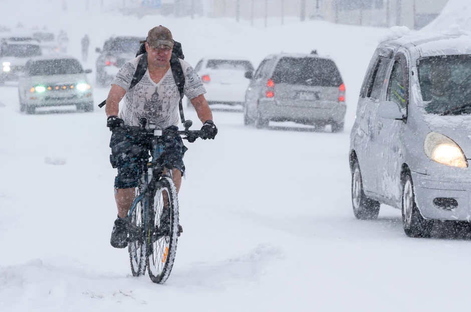 Rus vozi bicikl obučen u majicu dok je grad okovan snegom