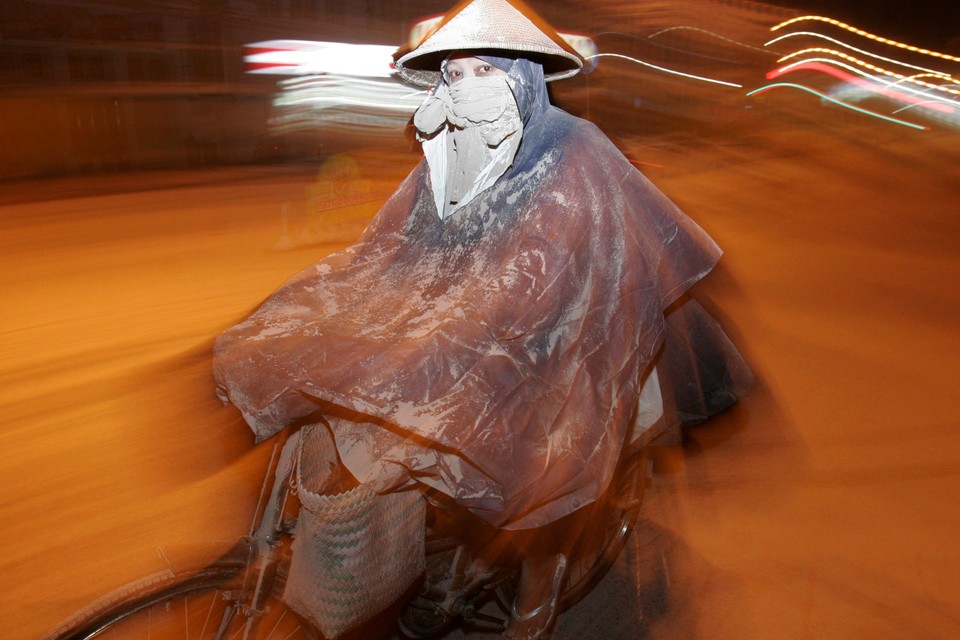 A woman wearing a rain coat rides a bicycle on an ash-covered road after another eruption of Mount Merapi volcano, in the city of Yogyakarta