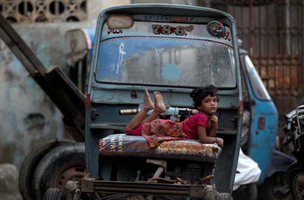 A girl rests on a rickshaw parked along a street in Karachi