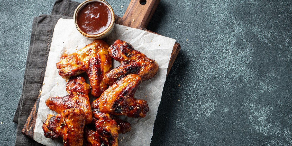 Roasted chicken wings in barbecue sauce with sesame seeds and parsley on a wooden board on a concret