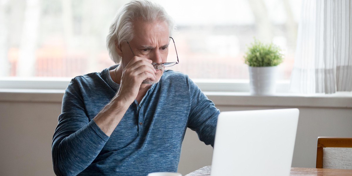 Shocked frustrated senior man taking off glasses looking at lapt