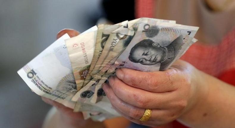 A vendor holds Chinese Yuan notes at a market in Beijing, August 12, 2015. REUTERS/Jason Lee