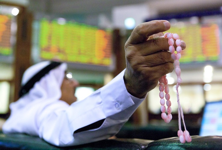 Mężczyzna trzyma modlitewne koraliki i obseruje notowania na giełdzie w Dubaju