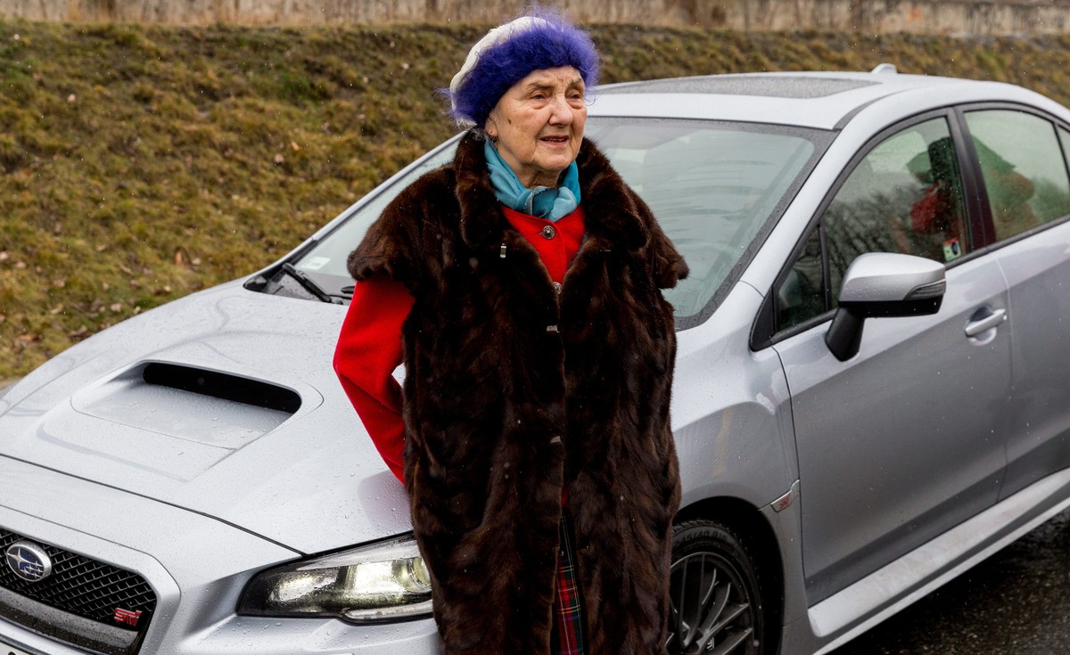 Na zdjęciu starsza kobieta w berecie i futrzanej kamizelce stoi przed srebrnym samochodem marki Subaru. Jakie warunki muszą spełnić seniorzy, aby posiadać prawo jazdy?