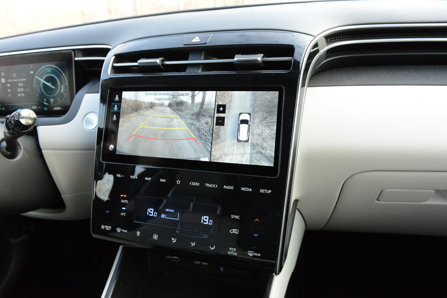 Hyundai Tucson wyposażony jest w system kamer, które bardzo uławiają manewry na parkingu. Pokazują obraz na ekranie systemu multimedialnego. Pod tym ekranem mamy zestaw przycisków, dzięki którym łatwo ustawimy klimatyzację albo wybierzemy dowolną stację radiową.