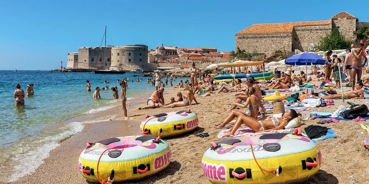 People on beach in Adriatic Sea and Dubrovnik fort