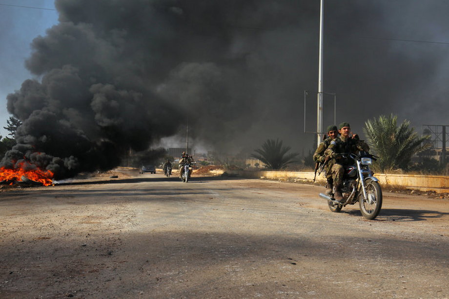 Rebel fighters drive their motorcycles under the smoke of burning tyres in Aleppo.