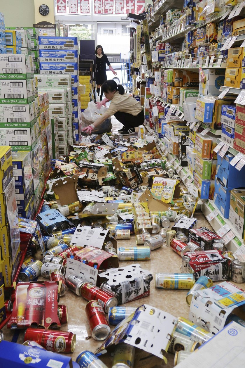 Employees try to remove bottles and cans of beverages which are scattered by an earthquake at a liqu