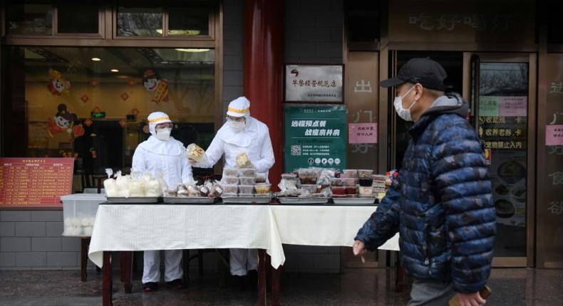 Restaurant workers wear protective clothing as they prepare food to sell on the street outside their restaurant in Beijing