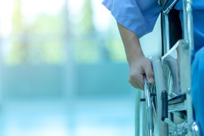 Asian disabled man is sitting in a wheelchair. He holds his hands on the wheel. Nearby are his colleagues, Medical equipment.