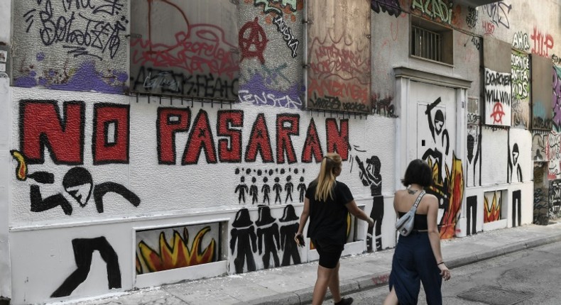 Women walk past a recent graffiti in Athens' historic district of Exarchia