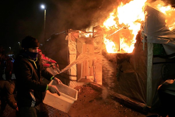 Migrants attempt to extinguish flames from a burning makeshift shelter set ablaze in protest against