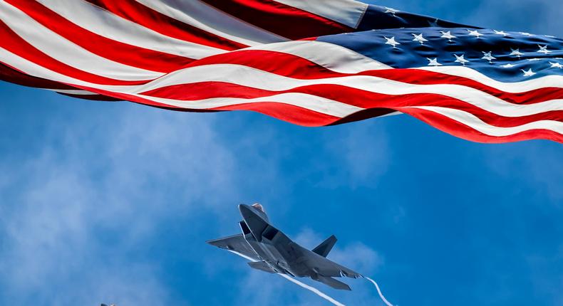 American flag blowing in wind and a Lockheed Martin F-22 Raptor flying against sky