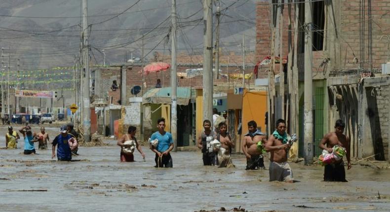 Residents of the town of Huarmey, 300 km north of Lima, wade through muddy water in the street after a flash flood hit the area the night before