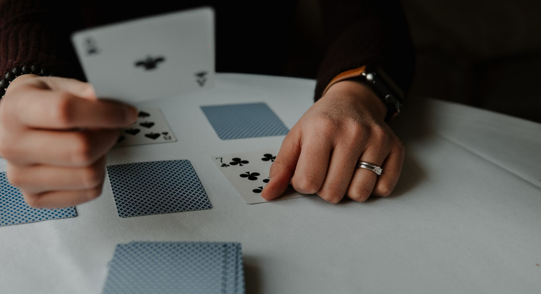 Person holding playing cards on white table [Unsplash]
