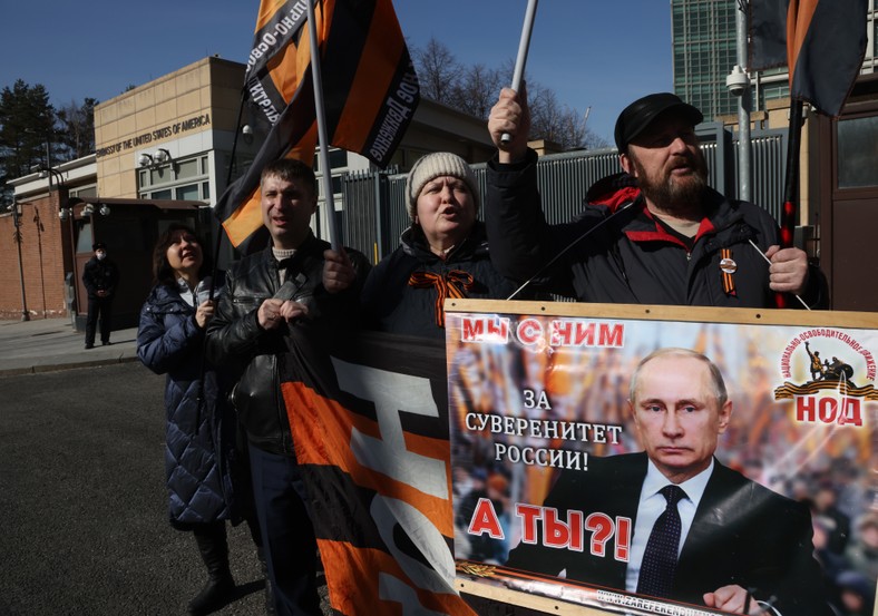 Aktywiści proputinowskiego Ruchu Wyzwolenia Narodowego trzymający plakat z wizerunkiem prezydenta Putina z napisem: "Jesteśmy z nim dla suwerenności Rosji. A wy?" podczas wiecu przed ambasadą USA, Moskwa, 19 marca 2023 r.