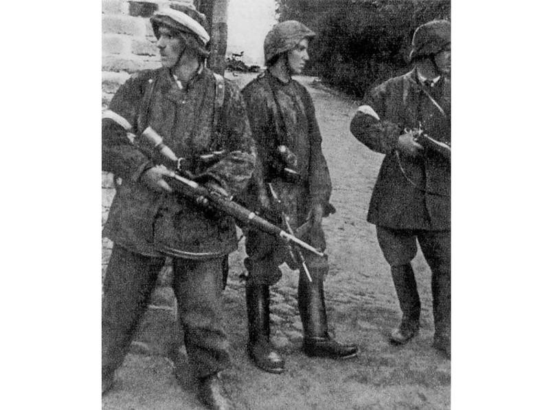 Patrol z II plutonu "Alek" 2. kompanii "Rudy" batalionu "Zośka" 5 sierpnia 1944 r. na Gęsiówce. Od lewej stoją: Wojciech Omyła "Wojtek", Juliusz Bogdan Deczkowski "Laudański" i Tadeusz Milewski "Ćwik". Milewski poległ na terenie "Gęsiówki" w dniu zrobienia tego zdjęcia; Omyła zginie trzy dni później. W chwilę po zrobieniu tego zdjęcia, w mur nad głowami powstańców uderzył niemiecki pocisk karabinowy - nikomu nic się nie stało