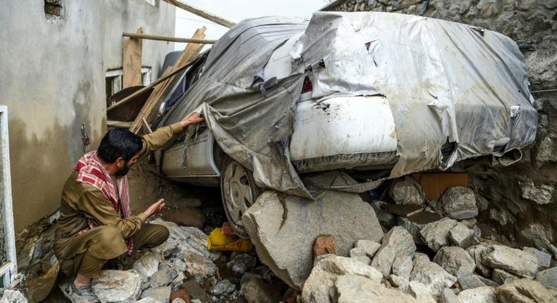 A villager inspects a damaged car among the debris of houses after a flash flood hit Charikar